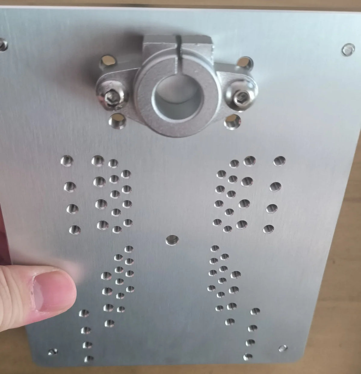 The plate held in a hand, showing the two clusters of tapped holes
